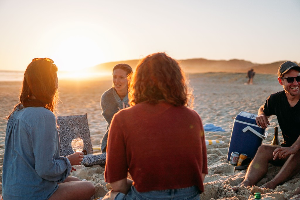Friends relaxing and laughing together on the beach at sunset